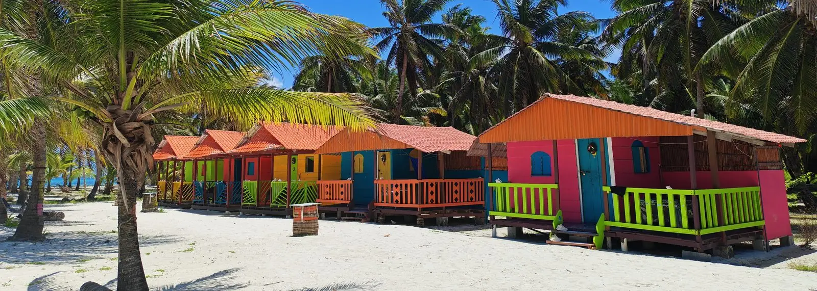 Cabañas de colores entre palmeras sobre la arena blanca