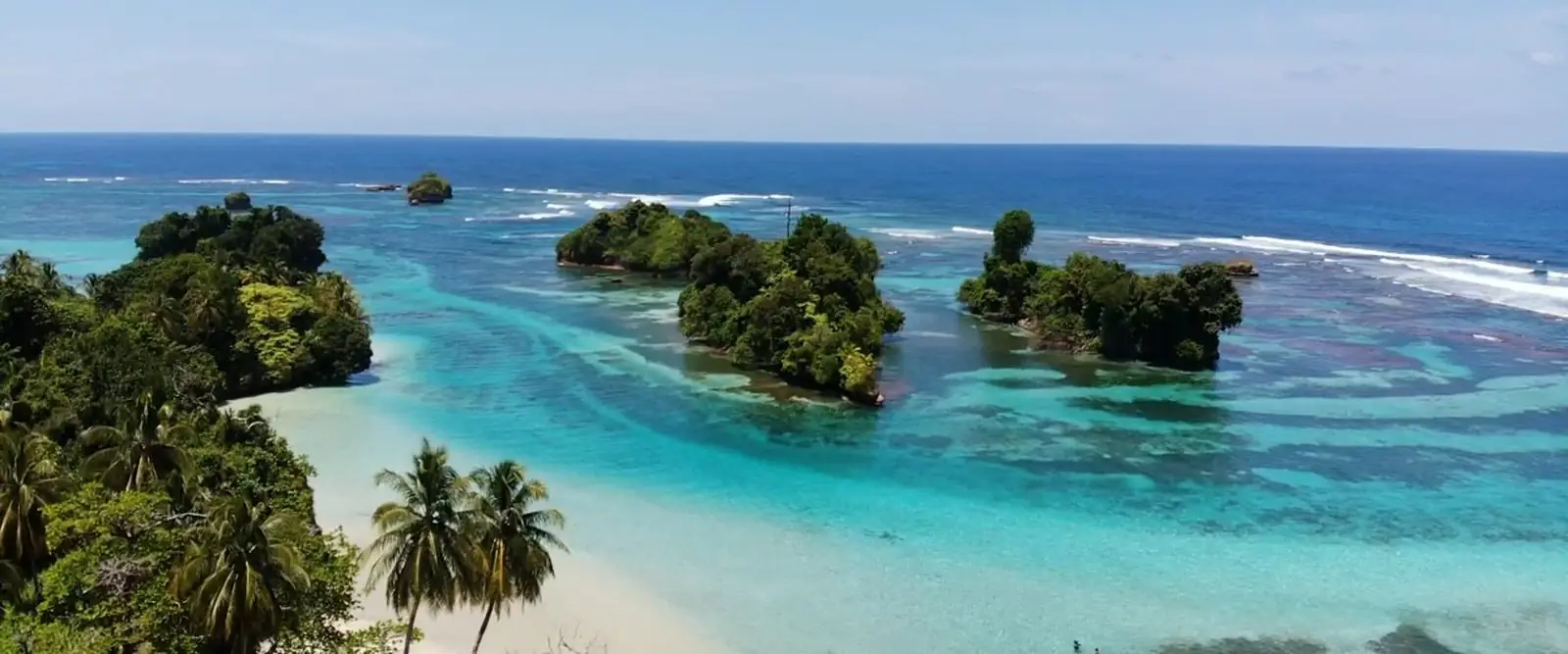Vista aérea de una playa con palmeras e islotes en aguas turquesas