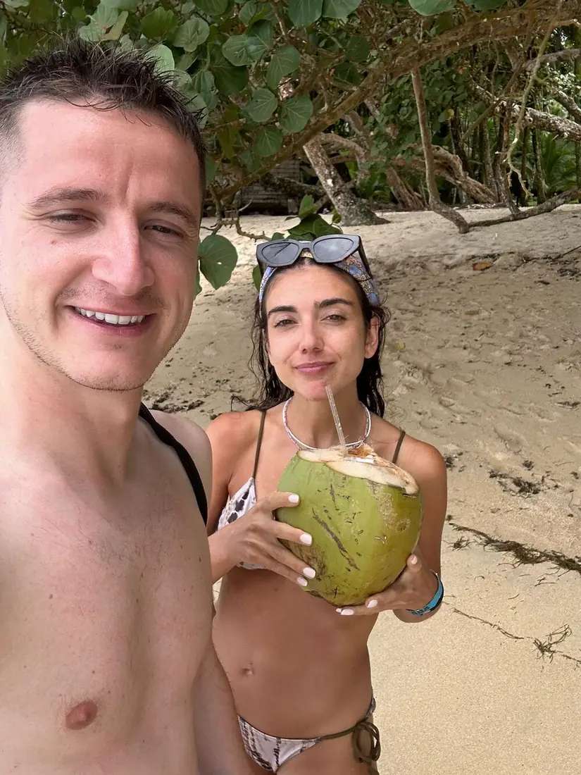 Pareja de viajeros haciéndose un selfi en la playa, ella con un coco