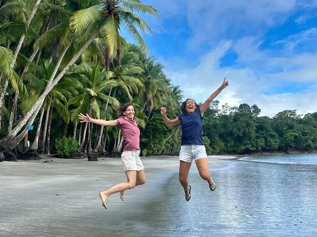 Dos viajeras saltando de alegría en una playa bordeada de palmeras