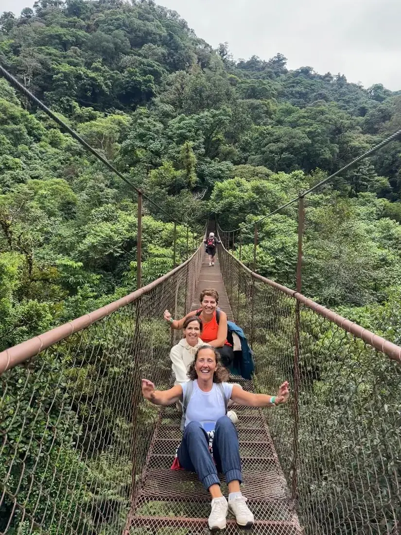Tres viajeras sentadas en un puente colgante sobre el bosque tropical