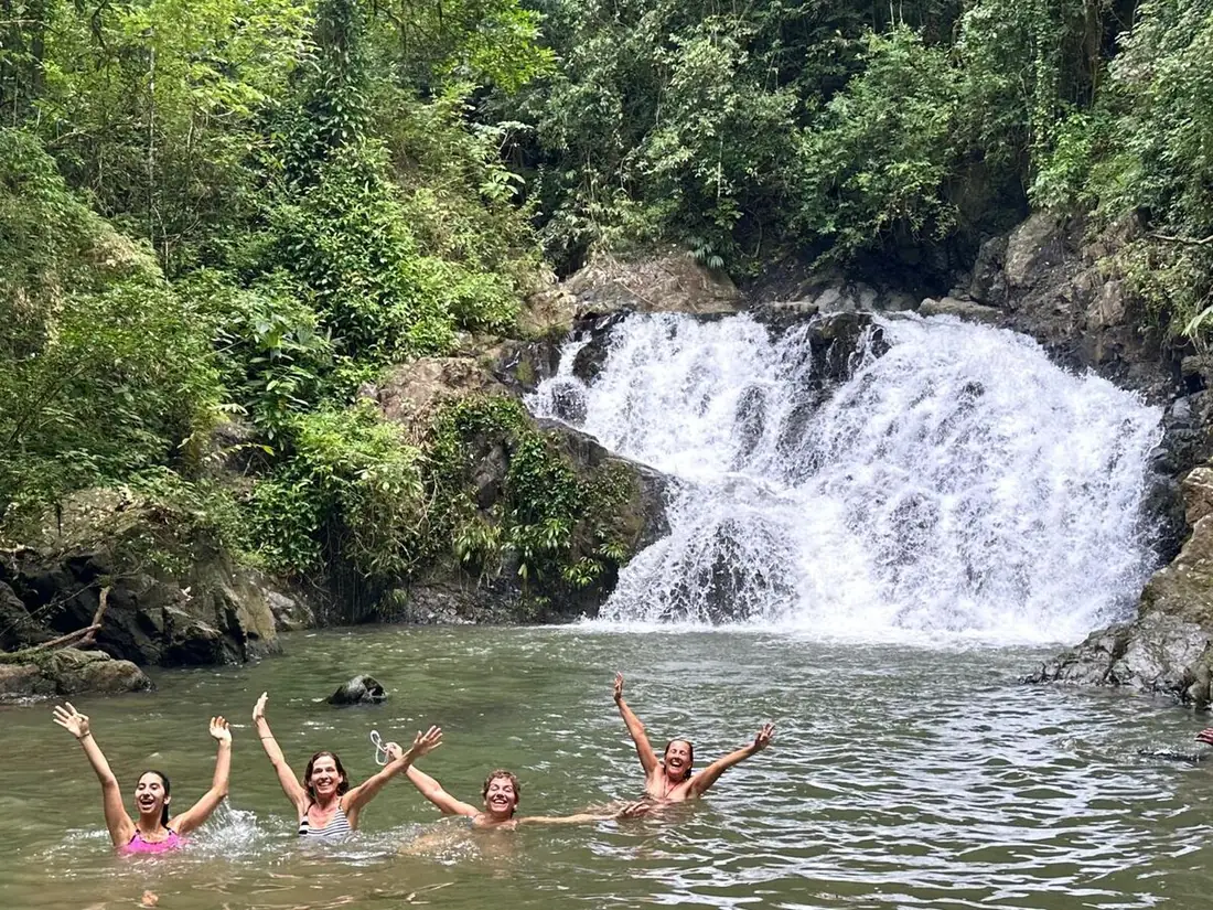 Cuatro viajeras bañándose con los brazos en alto frente a una cascada en la selva