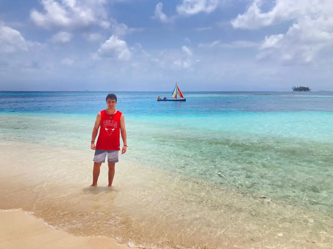 Viajero en la orilla de aguas turquesa con un velero guna de vela de colores al fondo