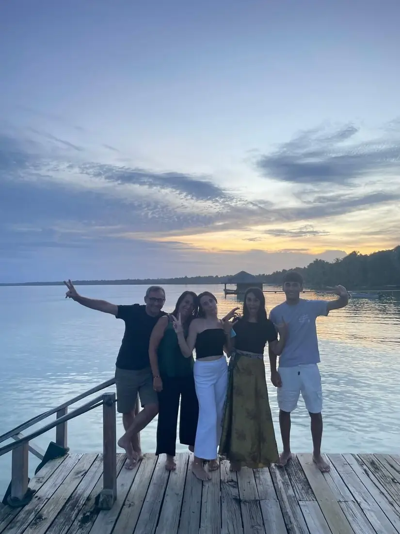 Familia de cinco saludando en un muelle al atardecer sobre el mar