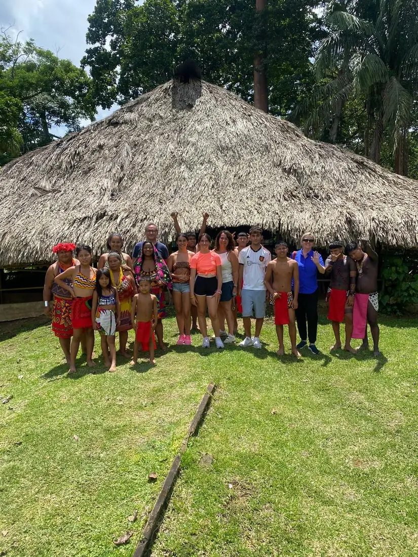 Familia junto a miembros de la comunidad emberá frente a una gran casa de techo de palma