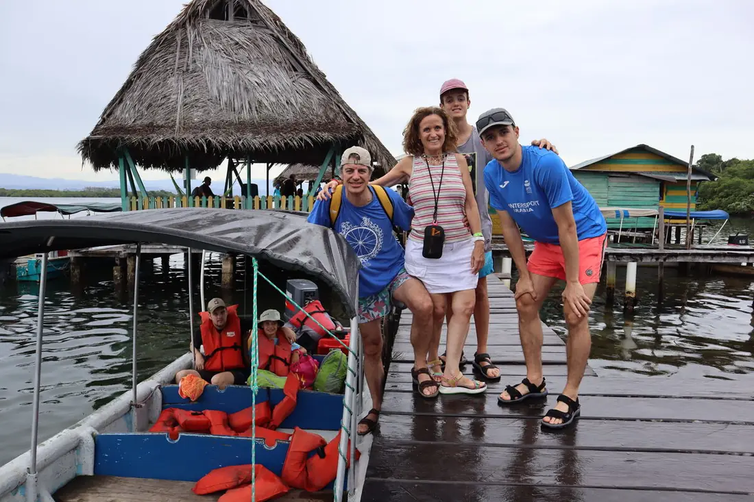 Familia en un muelle junto a una lancha y una cabaña de techo de palma en Bocas del Toro