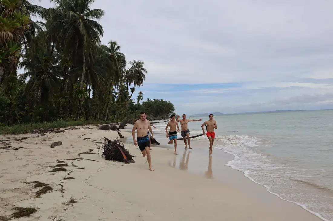Padre e hijos corriendo por una playa de arena blanca bordeada de cocoteros